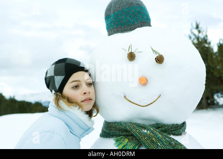 Teenage girl leaning against snowman, joue contre joue, portrait Banque D'Images