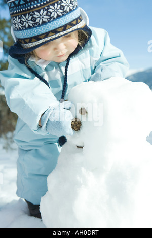 Bébé fille building snowman, vêtu de vêtements d'hiver Banque D'Images