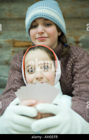 Girl holding cartes, smiling at camera, ami à ses cartes, à la fois habillé en vêtements d'hiver Banque D'Images