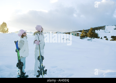 Deux jeunes amis se tenant ensemble, holding skis, looking away Banque D'Images