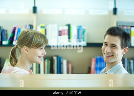 Deux étudiants dans la bibliothèque du campus à côté d'étagère, souriant, la tête et épaules Banque D'Images