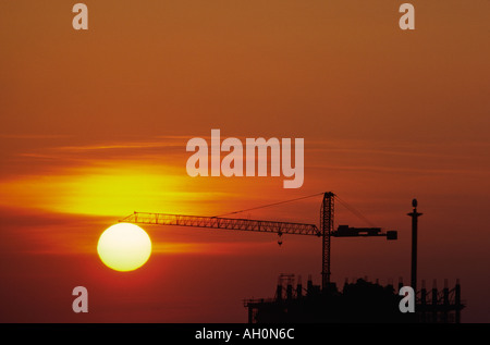 Sur un site de construction le soleil se couche derrière une grue assis sur le dessus de l'édifice thr Banque D'Images