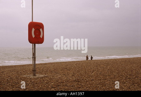 Homme et femme se rencontraient au bord de l'eau sur une plage déserte avec bouée de sauvetage à l'état Prêt. Banque D'Images