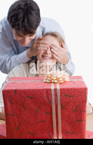 Close-up of a young man couvrant les yeux d'une jeune femme avec un cadeau en face d'eux Banque D'Images