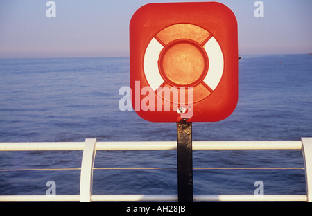 Close up of red pôle équipement de sauvetage par des garde-corps blanc donnant sur une mer de gonflement dans la lumière du soleil chaude avec lueur rose dans le ciel Banque D'Images