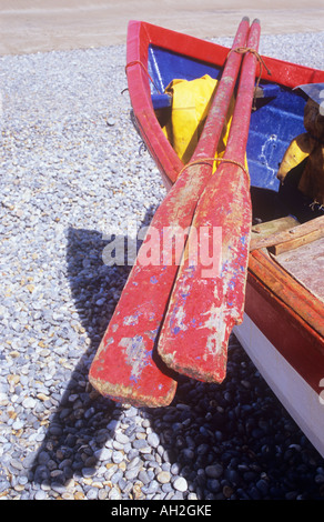 Détail d'avirons peint rouge arrimés sur un rouge bleu et blanc bateau de pêche avec bâche jaune pliée et échoué sur les cailloux gris Banque D'Images