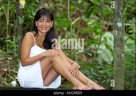 Asian woman smiling at the camera tout en étant assis au milieu de la jungle dans une robe blanche Banque D'Images