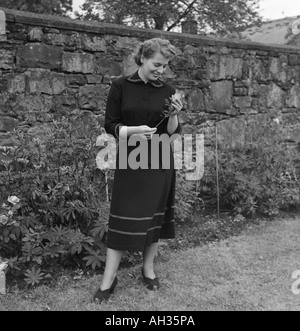 Vieille photo de famille (SNAP SHOT OF YOUNG WOMAN STANDING IN GARDEN HOLDING ROSE Banque D'Images