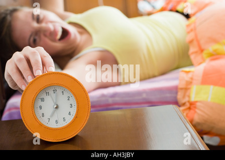 Jeune femme étendue sur le lit et de toucher un réveil Banque D'Images