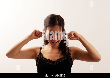 Jeune femme asiatique avec ses doigts dans ses oreilles afin de les protéger des niveaux de bruit douloureux de voir la douleur des sons excessive Banque D'Images