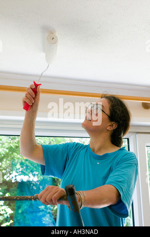 Femme à l'aide d'un rouleau pour peindre un plafond dans une maison au Pays de Galles Cardiff UK Banque D'Images