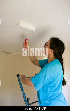 Femme à l'aide d'un rouleau pour peindre un plafond dans une maison d'habitation à Cardiff Wales UK Banque D'Images