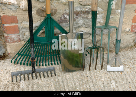 Outils de jardin bineuse bêche fourche et des râteaux appuyé contre un mur de toilettes extérieures Banque D'Images