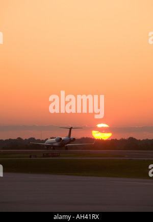 Un seul avion commercial attend sur une piste avec le soleil du matin à la hausse dans la distance. Banque D'Images