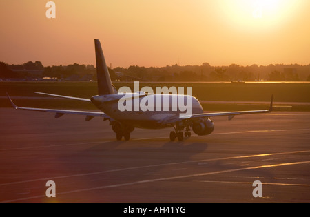 Un seul avion commercial attend sur une piste avec le soleil du matin à la hausse dans la distance. Banque D'Images