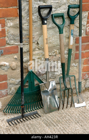 Outils de jardin bineuse bêche fourche et des râteaux appuyé contre un mur de toilettes extérieures Banque D'Images