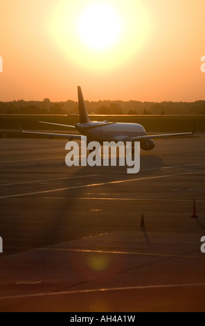 Un seul avion commercial attend sur une piste avec le soleil du matin à la hausse dans la distance. Banque D'Images