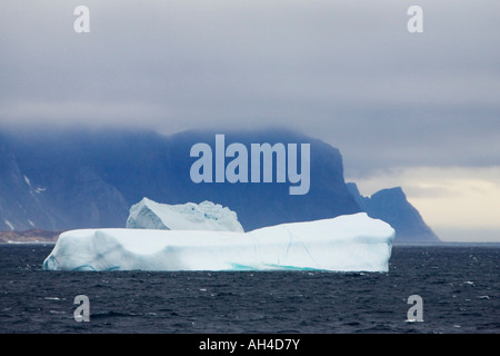 Montagnes spectaculaires sous faible ciel gris et lourd avec des icebergs blancs en revanche flottant à la mer au large de la côte sud-ouest du Groenland Banque D'Images