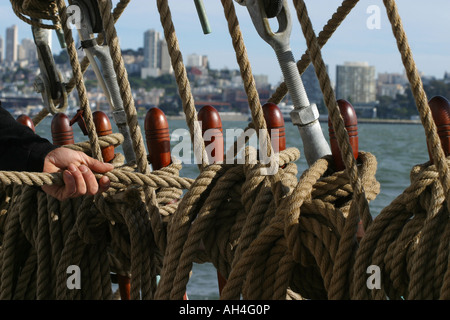 Part d'un marin en tirant sur la ligne autour de la détient à tirer vers le haut la voile dans un grand voilier naviguant sur la baie de San Francisco Banque D'Images