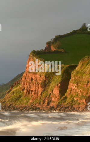 Les falaises de grès rouge s'illuminent par la lumière du soleil orageux juste après le lever du soleil, sur la plage de Ness, Shaldon, Devon, Grande-Bretagne. Banque D'Images