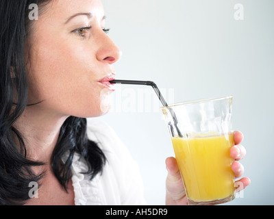 Femme buvant un grand verre de jus d'orange frais grâce à la paille Banque D'Images