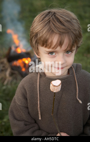 Cheeky Boy toasting marshmallows dans jardin à l'extérieur Banque D'Images