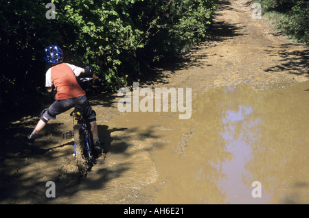 Garçon mal à cheval dans une flaque d'eau boueuse sur son vélo, Vitrolles-en-Luberon, Provence, France. Banque D'Images