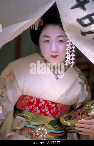 Une touriste habillée en maiko, ou apprentie geisha en formation, posant à un rideau de porte sur son chemin à l'extérieur, Kyoto, Japon. Banque D'Images