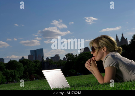 Jeune femme couchée en face d'un ordinateur portable dans un Park, New York City, New York, USA Banque D'Images