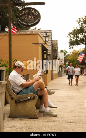 Homme caucasien senior lisant un journal tout en se relaxant sur un banc le long de la rue historique Aviles, composé Augustine, Floride, États-Unis. Banque D'Images