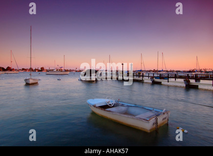 Un petit bateau rochers délicatement dans le port en face d'un coucher de soleil colorés sky Banque D'Images