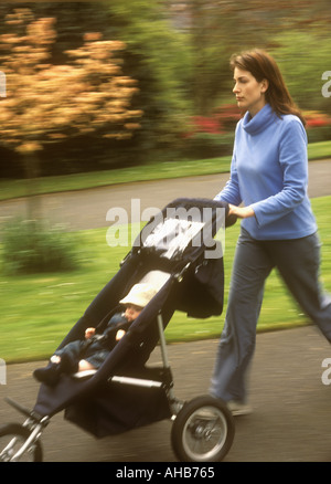 Mère poussant son bébé fils dans un pram dans un parc, Royaume-Uni Banque D'Images