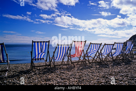 Une seule chaise longue rouge dans une rangée de chaises longues bleu dans le vent sur une journée ensoleillée à Beer Dorset Angleterre Banque D'Images