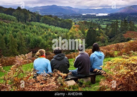 Quatre mi 20s randonneurs sur un banc sur le bas des pentes du Skiddaw à admirer la vue de Derwent Water, & Keswick Borrowdale. Banque D'Images