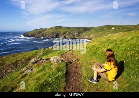 Une jeune femme assise sur l'herbe à Cape Cornwall sur Kenidjack Porth Ledden vers la tête. Près de St Just, Cornwall Banque D'Images