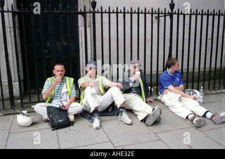 Groupe d'ouvriers prenant le déjeuner pause du travail sur la chaussée dans le centre de Londres. Banque D'Images