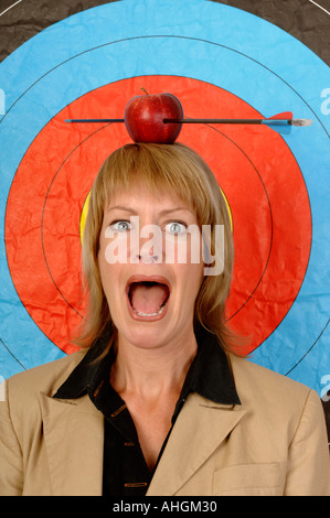 Businesswoman in front of une cible avec une pomme et la flèche sur la tête. Banque D'Images