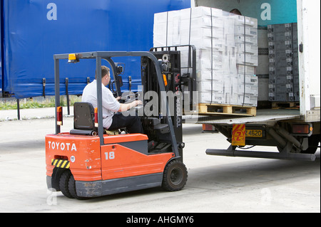 Ouvriers déchargement camion avec plateau élévateur chariot contenant palette enveloppée des piles de boîtes de système informatique Banque D'Images