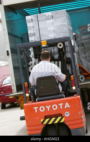 Ouvriers déchargement camion avec plateau élévateur chariot contenant palette enveloppée des piles de boîtes de système informatique Banque D'Images