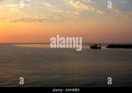 Petit bateau de pêche de quitter le port de calme au lever du soleil sur l'île de Corfou en Grèce Banque D'Images