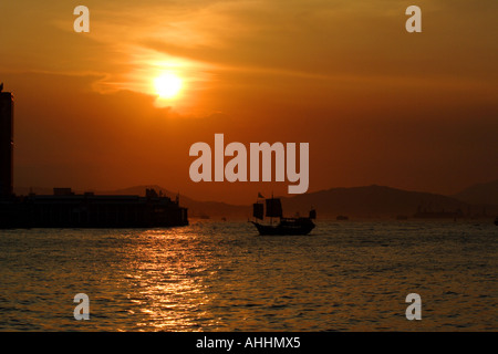 Vieille jonque chinoise en face d'un rouge doré Coucher du soleil dans le port de Victoria, Hong Kong Banque D'Images