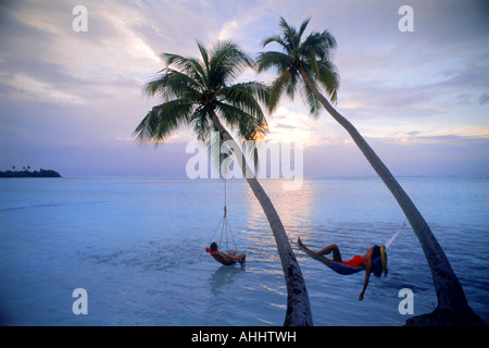 Couple hanging de palmiers de l'océan Indien aux Maldives au coucher du soleil Banque D'Images