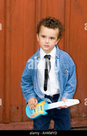 Jeune garçon portant des années 1950 outfit de maillot noir Cravate et veste en jean jouant un jouet guitare Banque D'Images