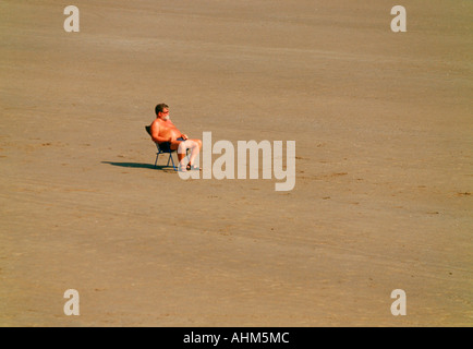 Un homme assis dans une chaise longue sur une plage déserte à Filey dans Yorkshire du Nord Banque D'Images