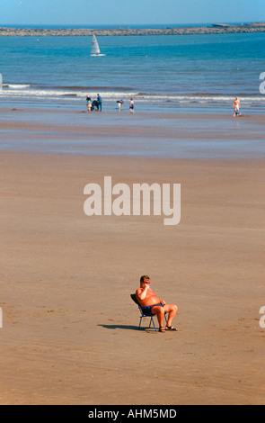 Un homme assis dans une chaise longue sur une plage déserte à Filey dans Yorkshire du Nord Banque D'Images