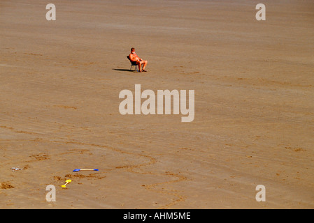 Un homme assis dans une chaise longue sur une plage déserte à Filey dans Yorkshire du Nord Banque D'Images