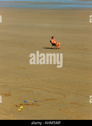 Un homme assis dans une chaise longue sur une plage déserte à Filey dans Yorkshire du Nord Banque D'Images