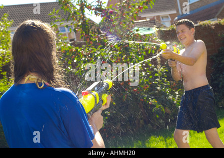 Teenage girl boy splashing chaque autres pistolets à eau dans un jardin Banque D'Images