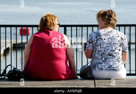 Deux femmes d'âge moyen assis bavardant au soleil donnant sur la baie de Cardiff South Wales UK Banque D'Images