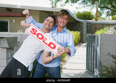 Gay couple holding sold sign in front of new house Banque D'Images